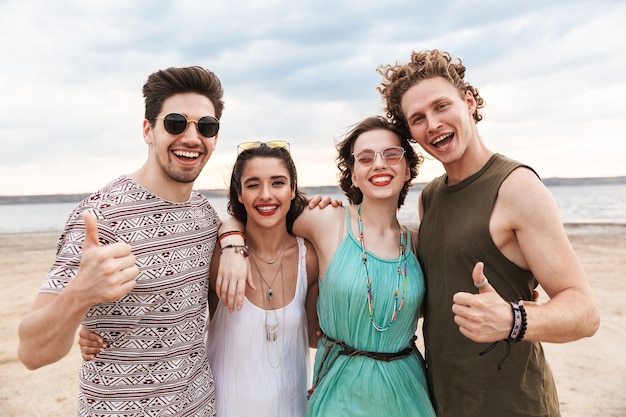 Groep vrolijke jonge vrienden die op het strand lopen, lachend