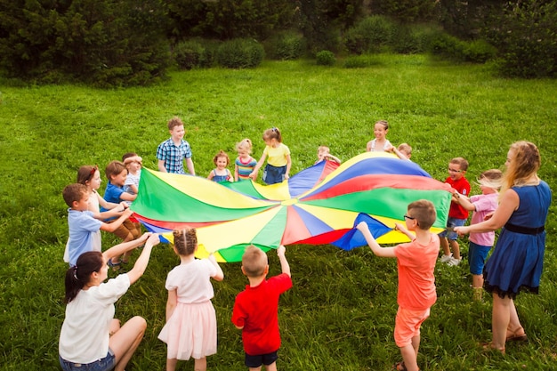 Groep vrolijke kinderen samen met leraren die buiten spelen met grote kleurrijke parachute Kinderen die golven maken met behulp van veelkleurige parachute Zomerkampideeën