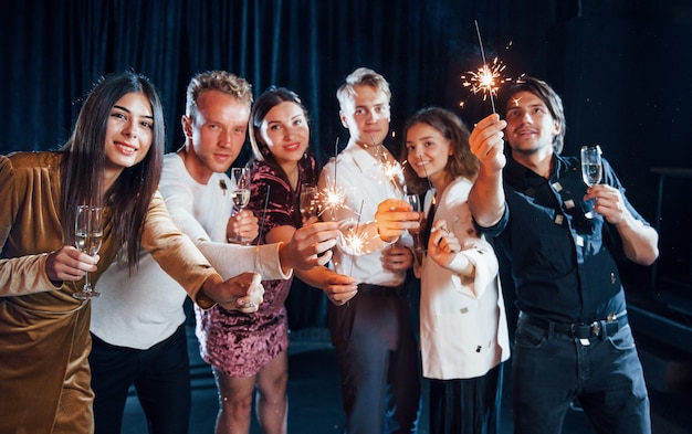 Groep vrolijke vrienden die nieuwjaar binnenshuis vieren met drankjes in handen.