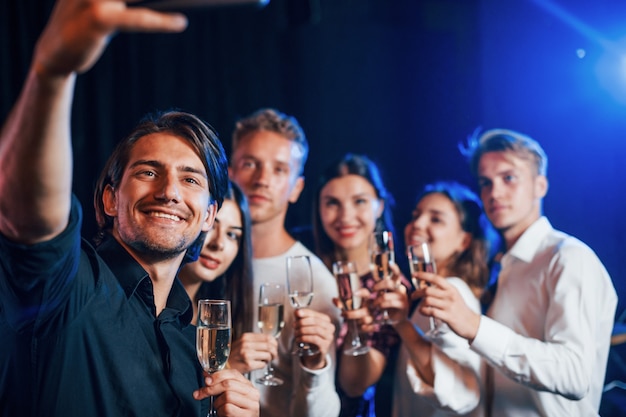 Groep vrolijke vrienden die nieuwjaar binnenshuis vieren met drankjes in handen.