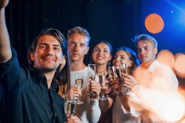 Groep vrolijke vrienden die nieuwjaar binnenshuis vieren met drankjes in handen.