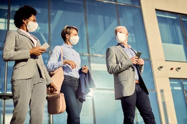 Groep zakelijke collega's met gezichtsmaskers die praten terwijl ze buiten lopen