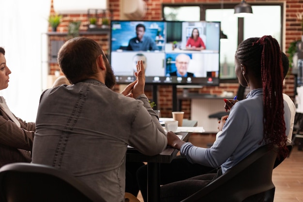 Groep zakenmensen die aan een bedrijfspresentatie werken en strategie-ideeën bespreken met managers op afstand tijdens een online videogesprekvergadering in het opstartkantoor. Zakelijke gespreksconferentie op monitor