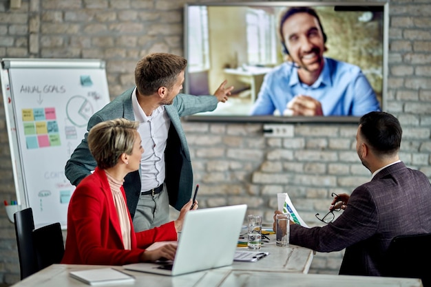 Groep zakenmensen die praten met hun collega die via videoconferentie deelneemt aan de vergadering