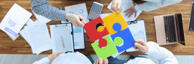 Groep zakenmensen zitten aan tafel en stellen kleurrijke puzzel bovenaanzicht samen