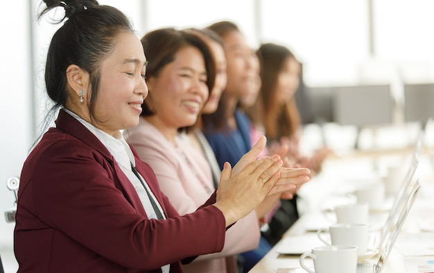 Groep zakenvrouwen in pak zitten aan een bureau en klappen in de handen voor het waarderen aan iemand in een modern kantoorbedrijf. Concept van goede omstandigheid in gezelschap met vrienden en collega's.