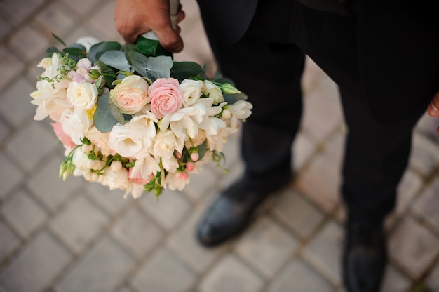 Groom in a black suit and classic shoes holding a wedding bouquet
