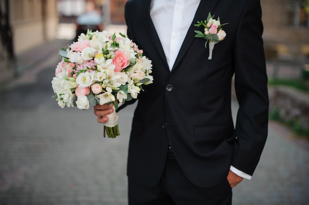 Groom in a black suit holding a gentle wedding bouquet