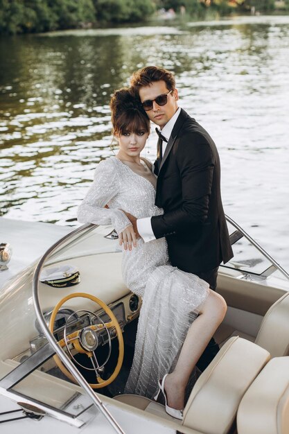 Groom in a black suit and sunglasses hugs bride in wedding dress on a yacht on a sunny day