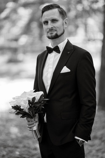 Groom in a black suit with a bow tie in a city park