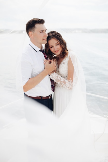 Photo groom in black suit with bride in long white dress ride on a large white yacht together