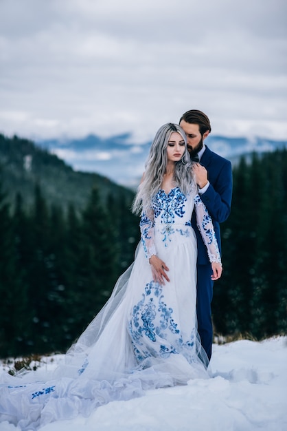 Groom in a blue suit and bride in white, embroidered with blue pattern