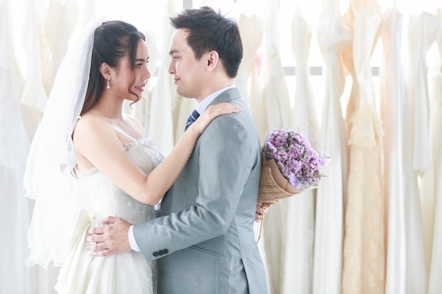 Жених и невеста стоят, улыбаются и обнимаются на фоне платья невесты. Женщина, держащая фиолетовый букет, олицетворяет любовь к мужчине. Концепция свадьбы лучший день.