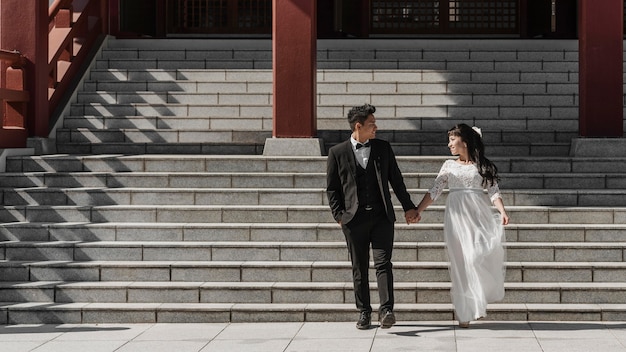 Photo groom and bride holding hands while coming down the stairs