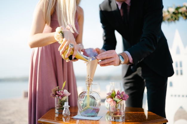 Lo sposo e la sposa versano la sabbia multicolore a strati in un barattolo di vetro