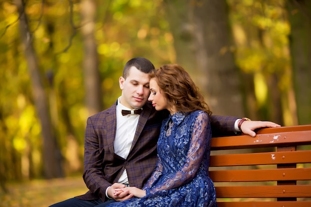 Groom and Bride sitting on bench in a park. wedding dress.