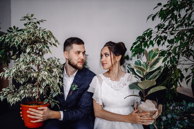 Groom and bride sittting and looking each other and holding two green plants