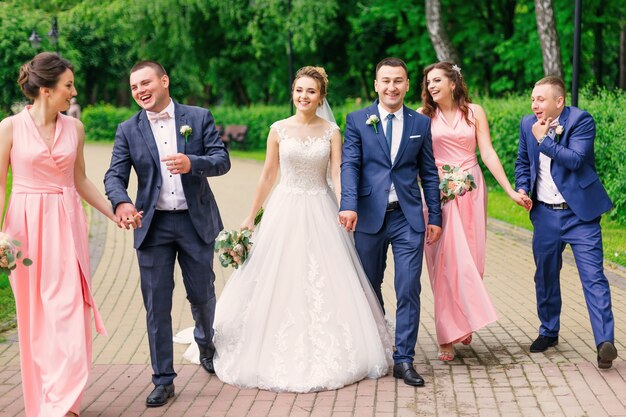 Groom and bride walk with groomsman and bridesmaid in the park.