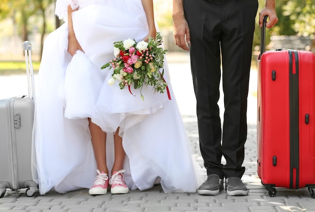 Groom and bride with suitcases walking in park