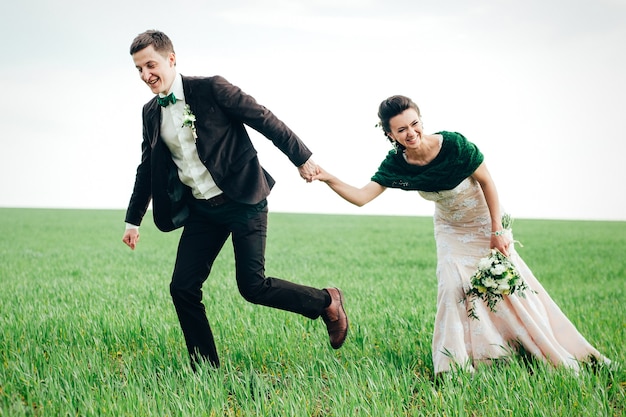 The groom in a brown suit and the bride in an ivory-colored dress on a green field receding into the distance against the sky