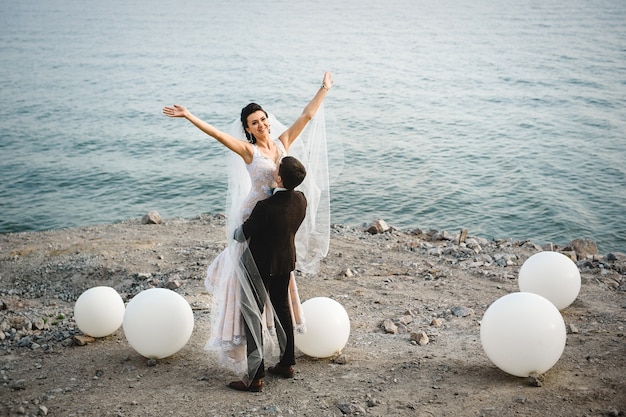 The groom in a brown suit and the bride in an ivory dress on the rocky seashore