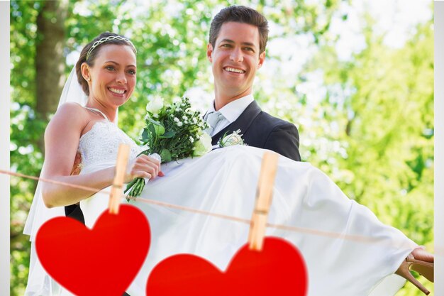 Groom carrying bride in garden against hearts hanging on a line