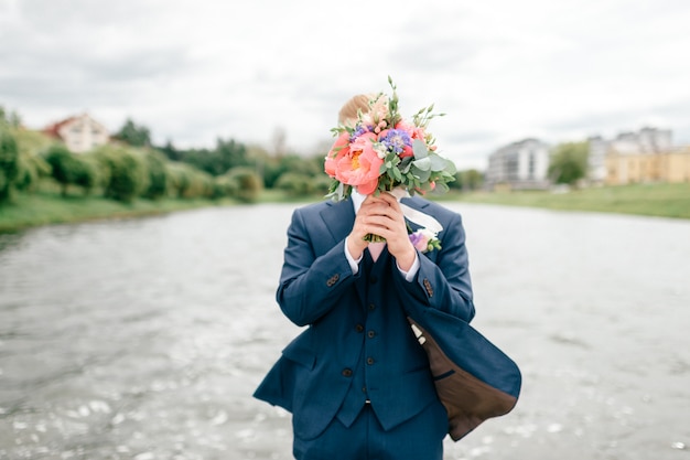 Groom covering his face with wedding bouqet of flowers
