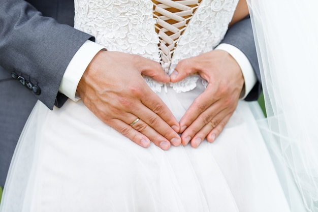 Groom embrace his bride and makes the shape of the heart from his hands with wedding ring