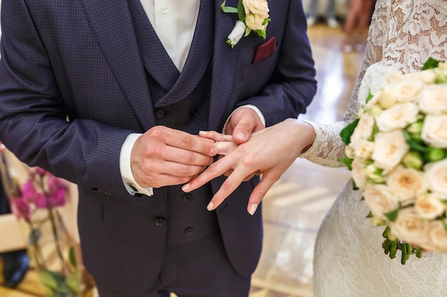 Groom embraces the bride with wedding bouquet with violet rose\
groom dresses an engagement ring to the bride newlyweds exchange\
wedding rings