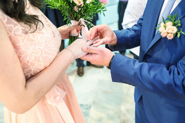 Groom embraces the bride with wedding bouquet with violet rose\
groom dresses an engagement ring to the bride newlyweds exchange\
wedding rings