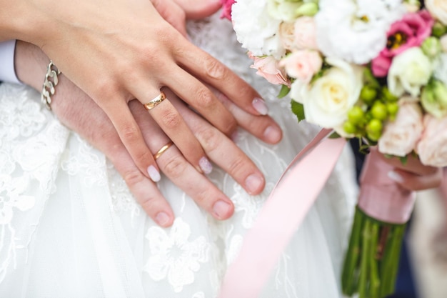 Groom embraces the bride with wedding red white rose bouquet rings on the hands of newlymarried couple