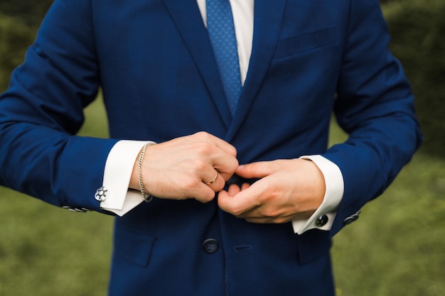 The groom fastens a button on a blue jacket closeup