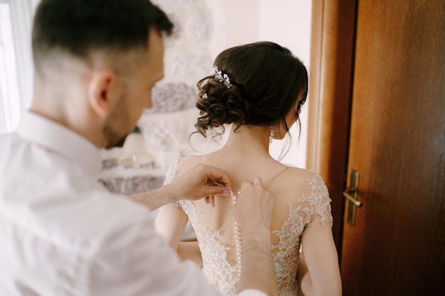 Groom fastens the buttons on the brides dress closeup