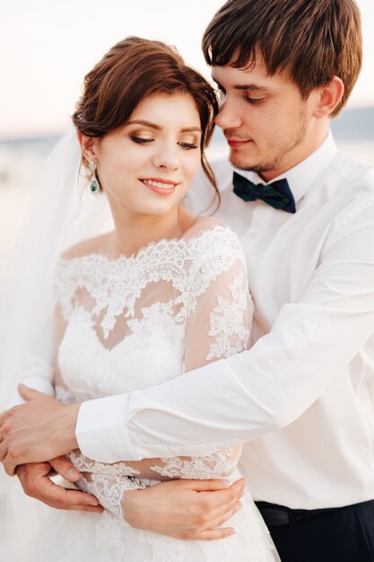 The groom gently hugs the bride from behind