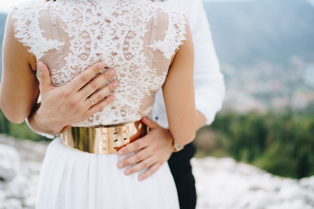 Lo sposo abbraccia delicatamente le mani della sposa dello sposo sulla vita del primo piano della sposa