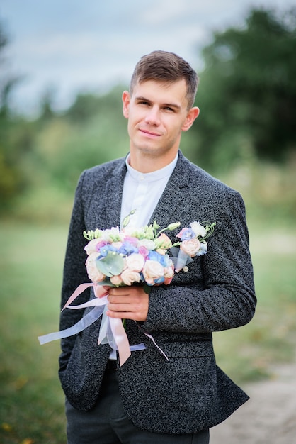 グレースーツの新郎はカラフルな結婚式の花束を保持
