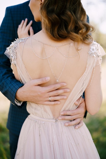 Groom hands hug bride lower back back view closeup