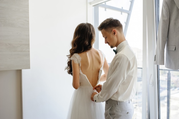 The groom helps to fasten the dress to his bride.