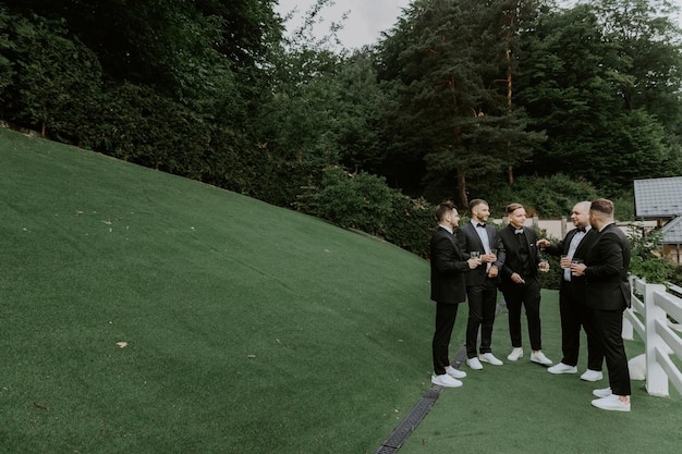 groom and his groomsmen friends in stylish suits drinking whiskey outdoor