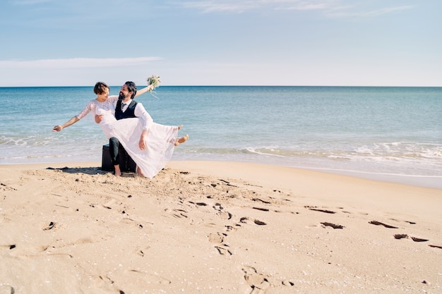 写真 海岸でのビーチウェディングで花嫁を腕に抱く新郎