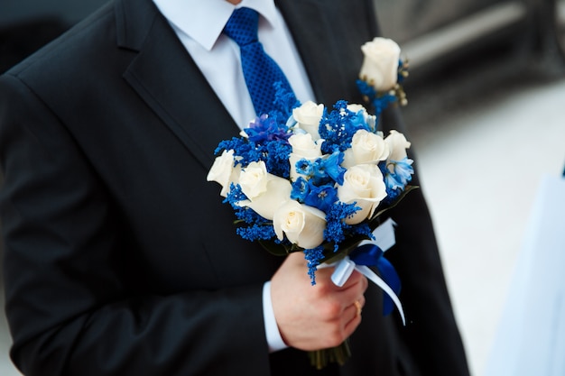 Groom holding creative winter wedding bouquet of fresh white roses and delphinium