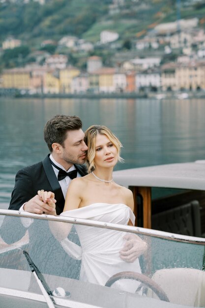 Foto lo sposo tiene la mano della sposa abbracciandole la vita mentre si trova su un motoscafo sul lago di como, italia