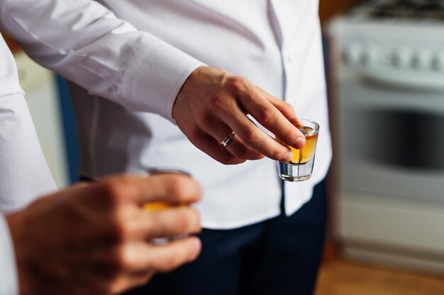 The groom holds a glass of alcohol in his hand and celebrates with his friends in the kitchen