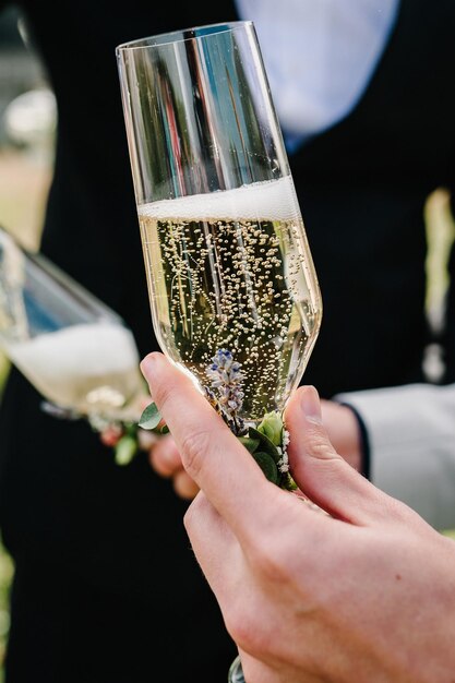 The groom holds a glass of champagne on the background of the friends on nature at the wedding ceremony Close up Toast