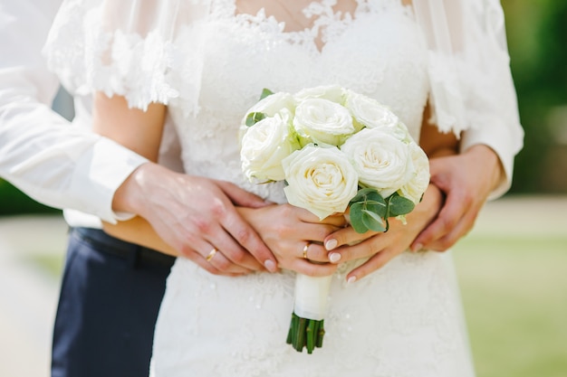彼女は白いバラの結婚式の花束を保持している間、新郎新婦は花嫁の1つに手を保持しています