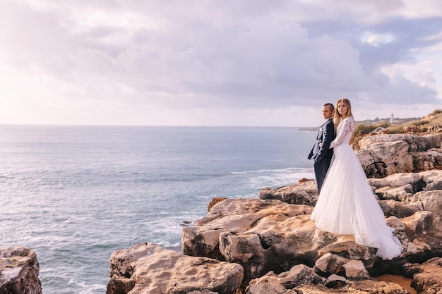 Groom holds his hands in his pockets and looks at the ocean the