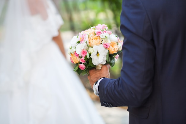 The groom holds the wedding bouquet of flowers