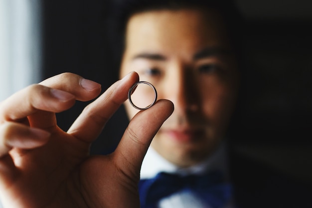 Photo groom holds wedding ring before his eye