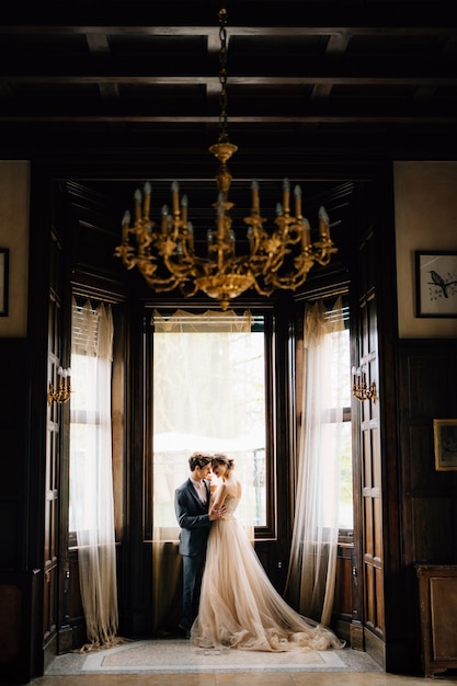 Photo groom hugs bride against the background of the large windows