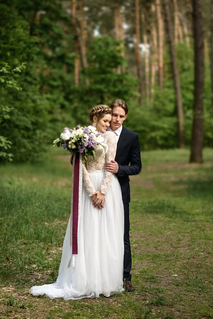 The groom hugs the bride from behind in the forest